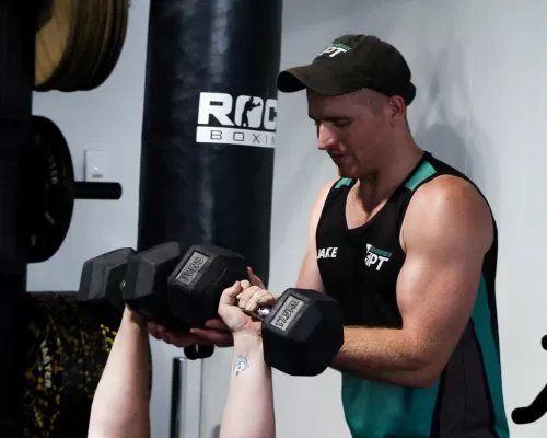 a woman lifting waits with a help of a personal trainer